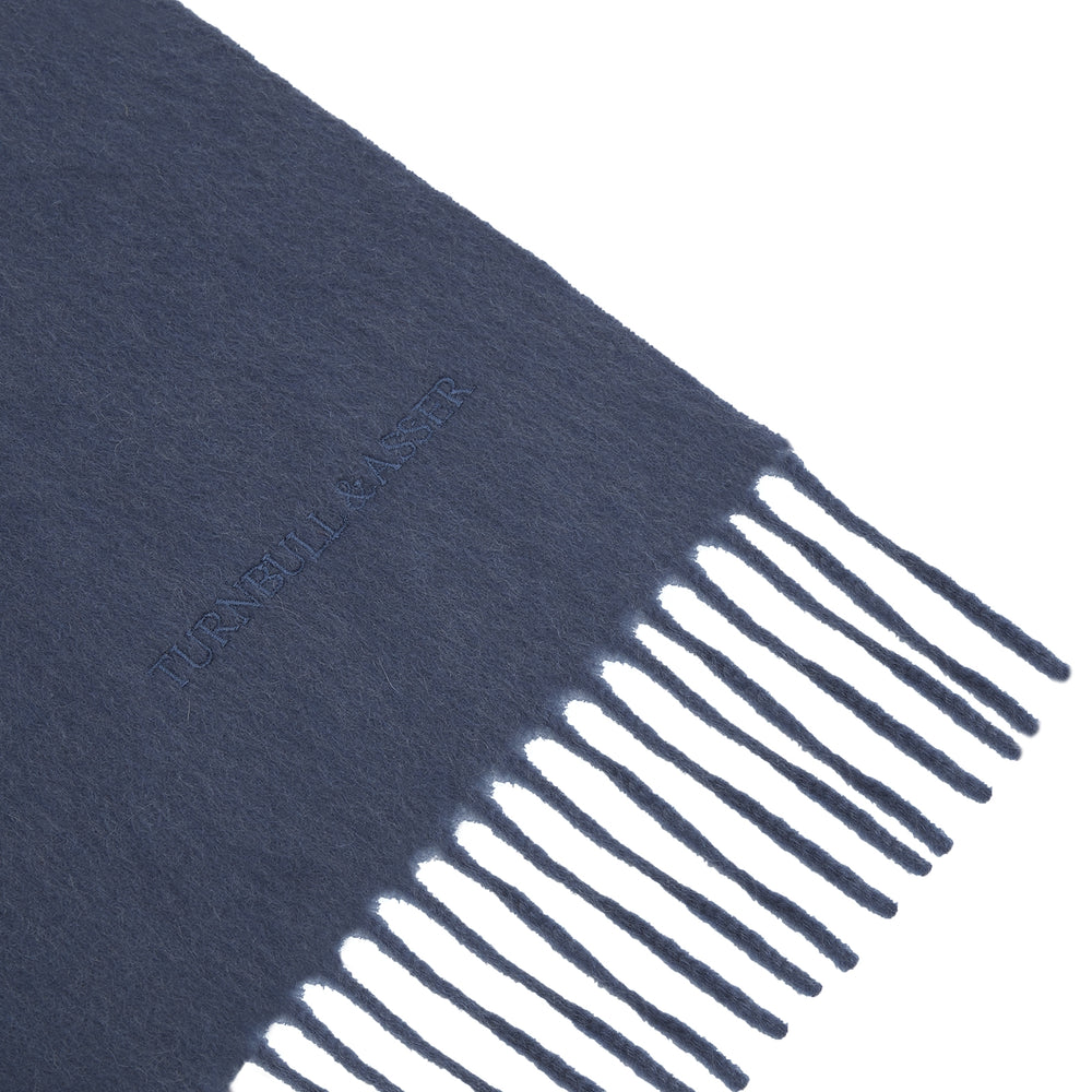 The Turnbull & Asser Slate Pure Cashmere Scarf is a luxurious navy blue accessory with fringed ends, neatly folded and showcased on a plain white background.
