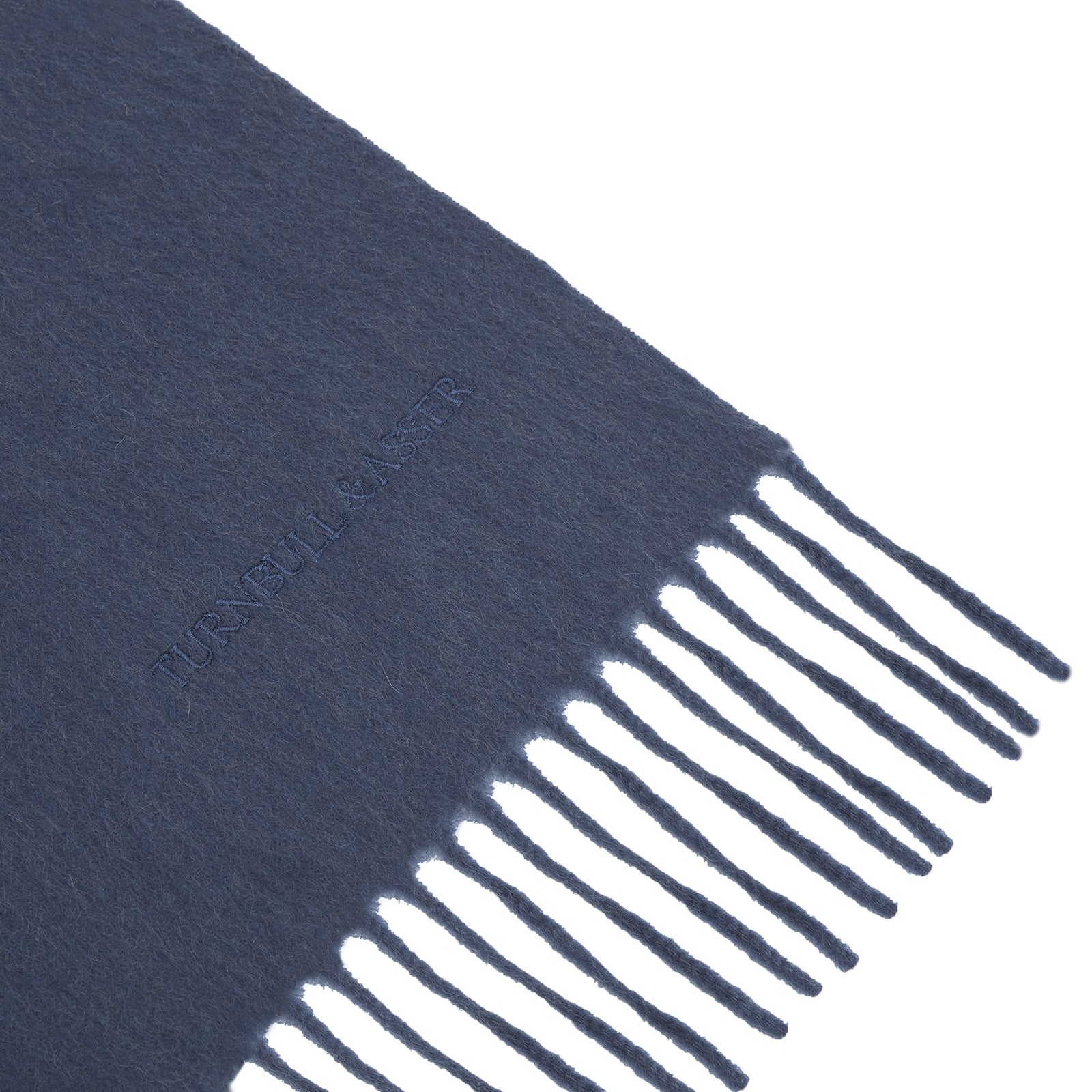 View 2 of product The Turnbull & Asser Slate Pure Cashmere Scarf is a luxurious navy blue accessory with fringed ends, neatly folded and showcased on a plain white background.