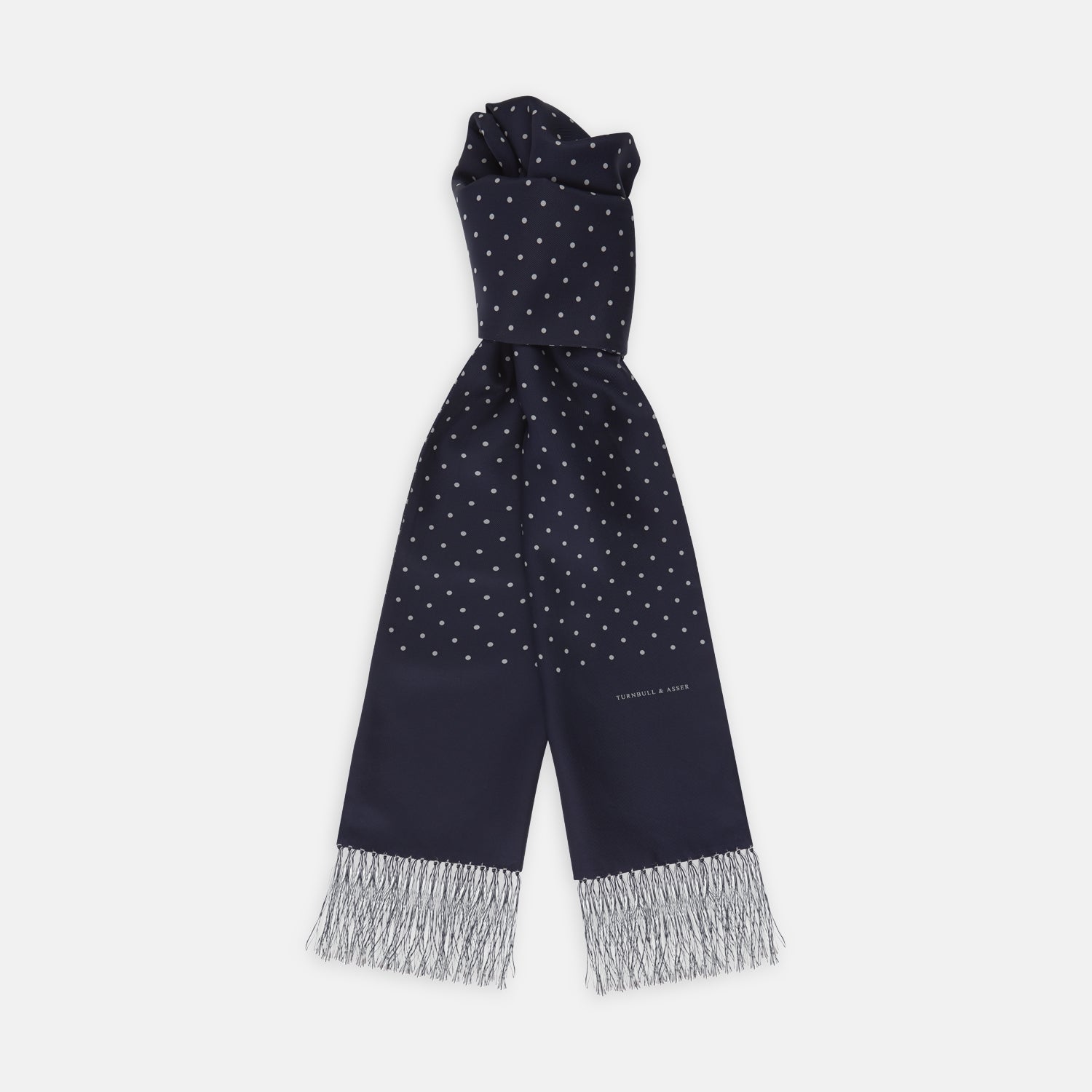 View 1 of product The Turnbull & Asser Navy and White Spotted Silk Scarf with Fringes, featuring small polka dots and grey fringe at both ends, is neatly folded and displayed on a plain white background.