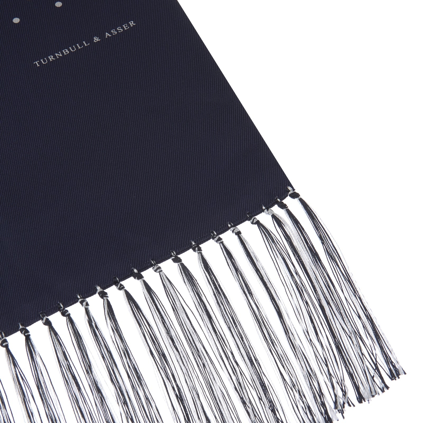 View 2 of product The Turnbull & Asser Navy and White Spotted Silk Scarf with Fringes, featuring small polka dots and grey fringe at both ends, is neatly folded and displayed on a plain white background.