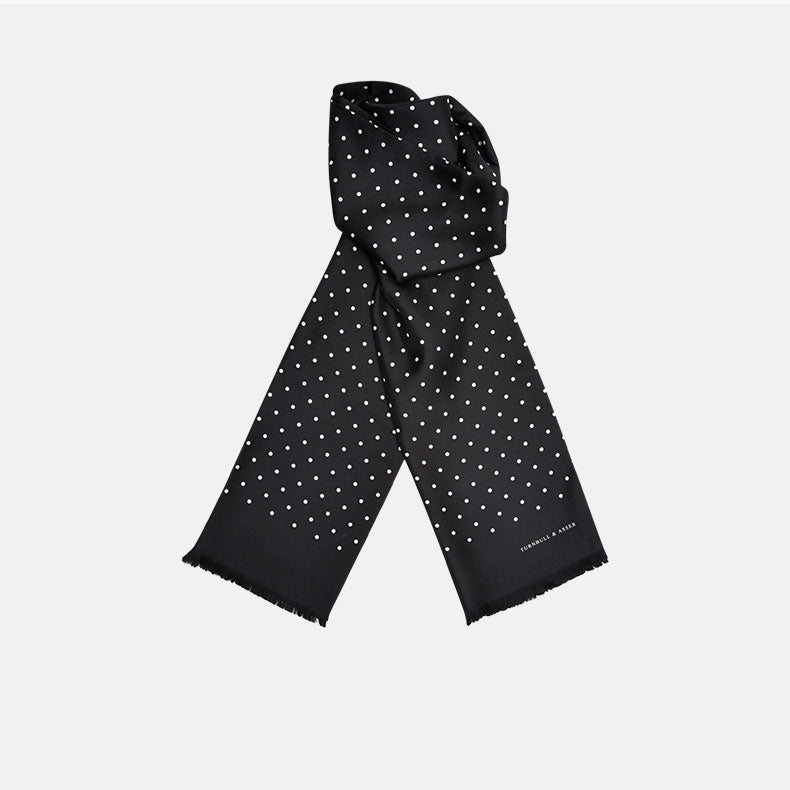 The Black and White Spotted Silk Scarf by Turnbull & Asser features small hand-printed white polka dots and short fringes, shown laid flat on a white background.