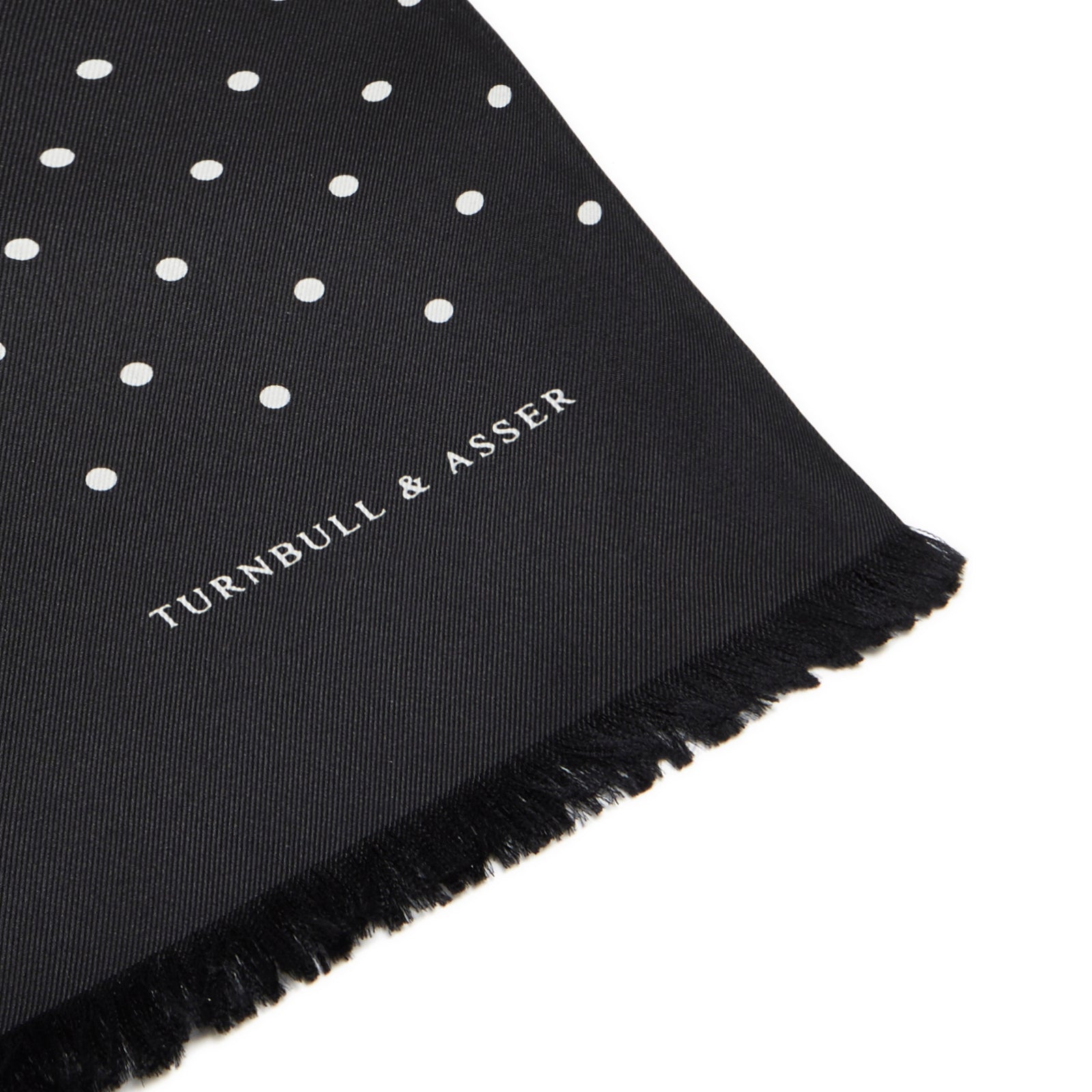 View 2 of product The Black and White Spotted Silk Scarf by Turnbull & Asser features small hand-printed white polka dots and short fringes, shown laid flat on a white background.