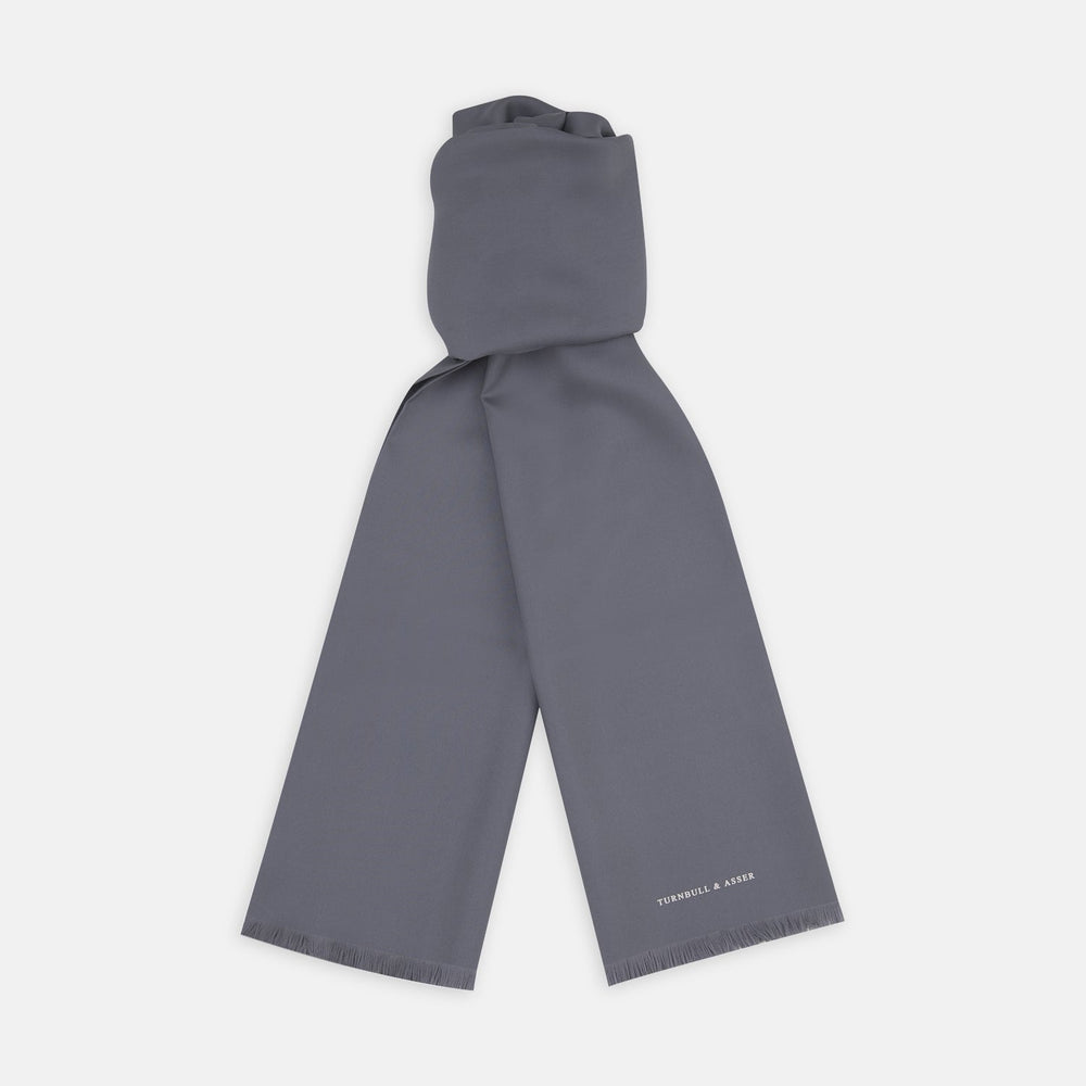 The Plain Grey Silk Scarf by Turnbull & Asser features fringed edges and the brand name in white near one end, neatly folded and elegantly displayed on a plain white background.