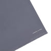 View 2 of product The Plain Grey Silk Scarf by Turnbull & Asser features fringed edges and the brand name in white near one end, neatly folded and elegantly displayed on a plain white background.