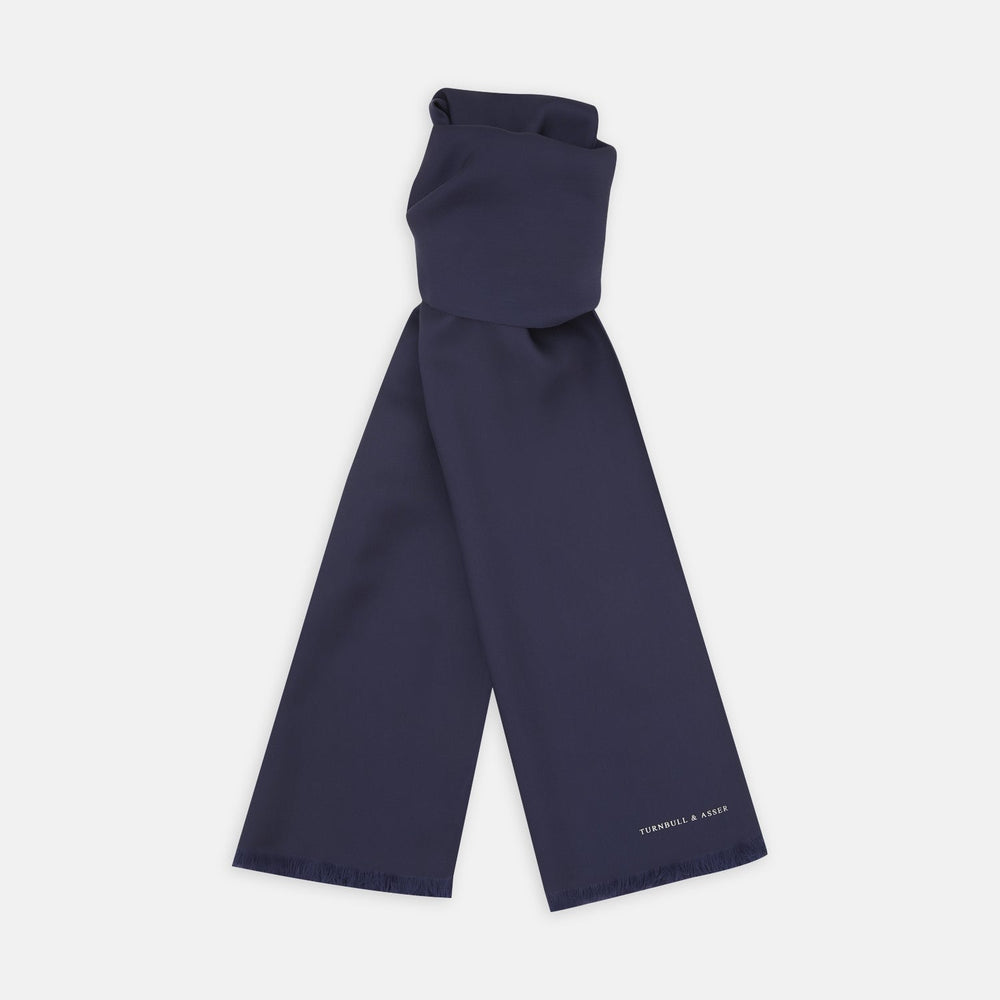 A Plain Navy Silk Scarf by Turnbull & Asser, neatly folded with both ends hanging down, is shown against a white background. One end displays subtle white branding, highlighting this elegant accessory.