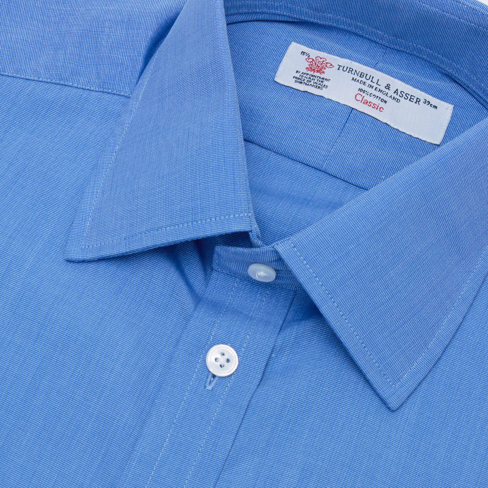A neatly folded, dark blue end-on-end men's dress shirt by Turnbull & Asser, featuring a T&A collar and double cuffs, is displayed against a plain white background.
