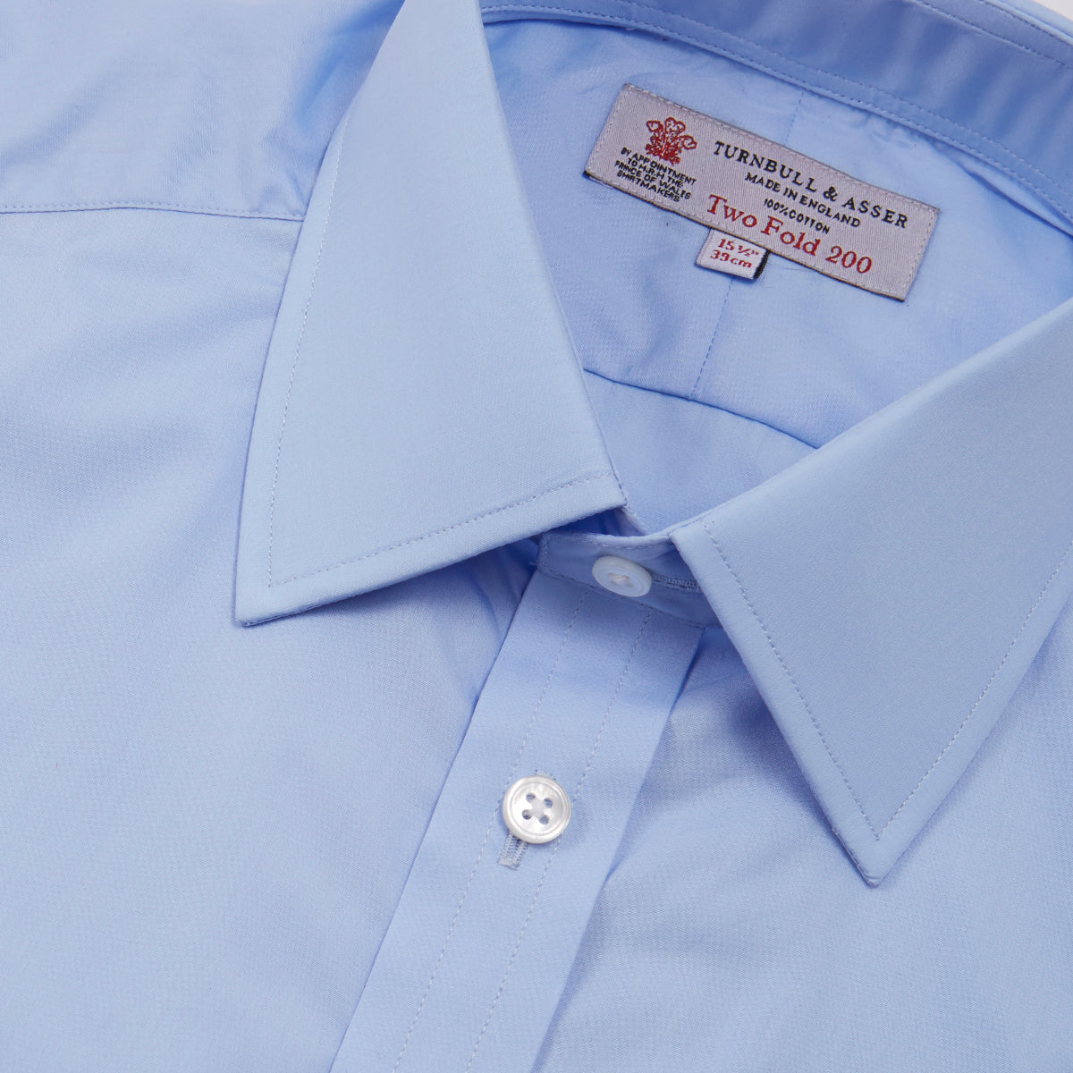 View 5 of product The Turnbull & Asser Two-Fold 200 Blue Cotton Shirt features a T&A collar, double cuffs, white buttons, and a visible label inside the collar, displayed neatly folded on a plain white background for superior breathability.