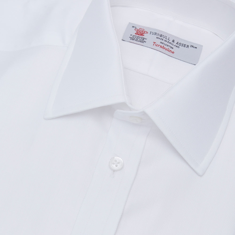 The Turnbull & Asser White Herringbone Superfine Cotton Shirt features a T&A collar and 3-button cuffs, displayed against a light blue background—ideal for minimalist styles or pairing with bold ties.