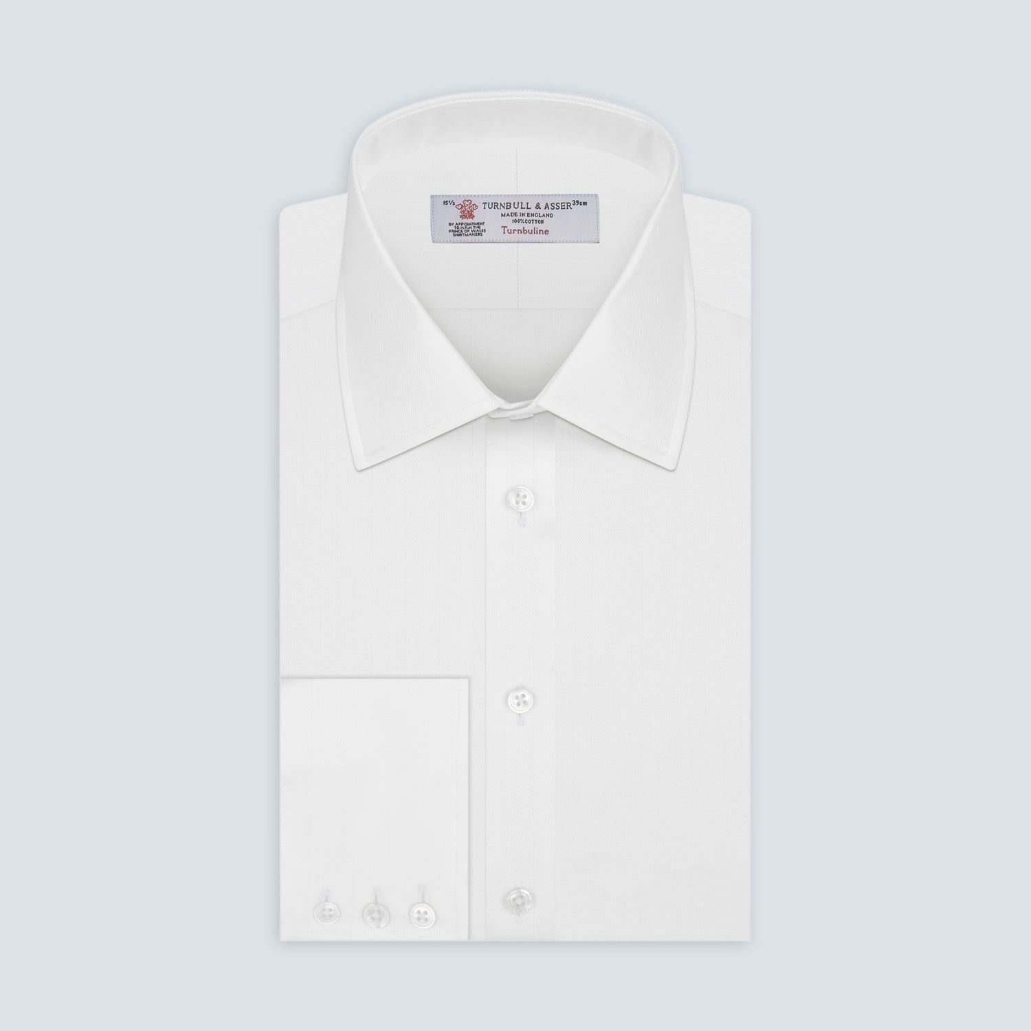 View 1 of product The Turnbull & Asser White Herringbone Superfine Cotton Shirt features a T&A collar and 3-button cuffs, displayed against a light blue background—ideal for minimalist styles or pairing with bold ties.