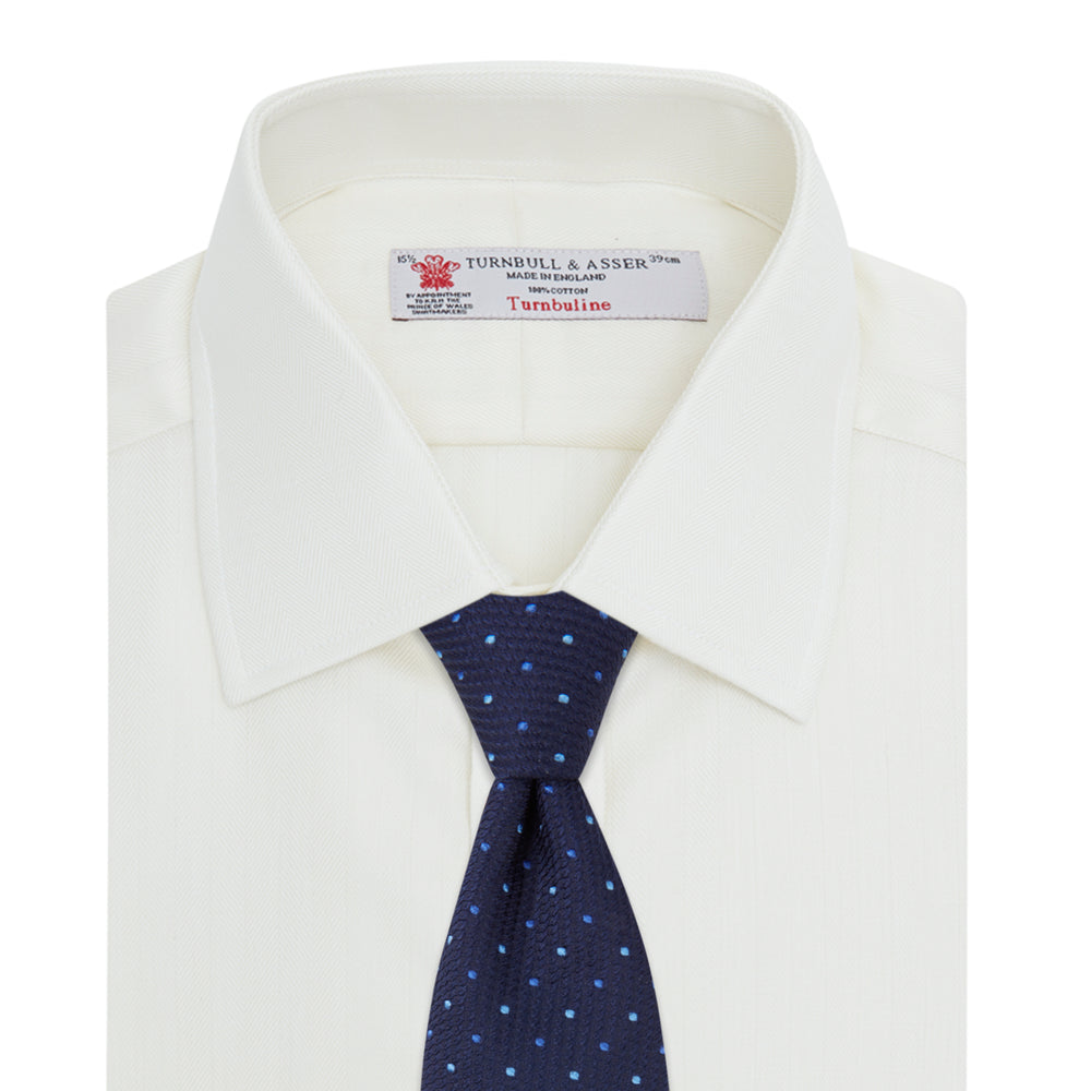 The Turnbull & Asser Cream Herringbone Superfine Cotton Shirt features a T&A collar and 3-button cuffs, ideal for minimalist style or bold ties, shown neatly folded against a plain white background.