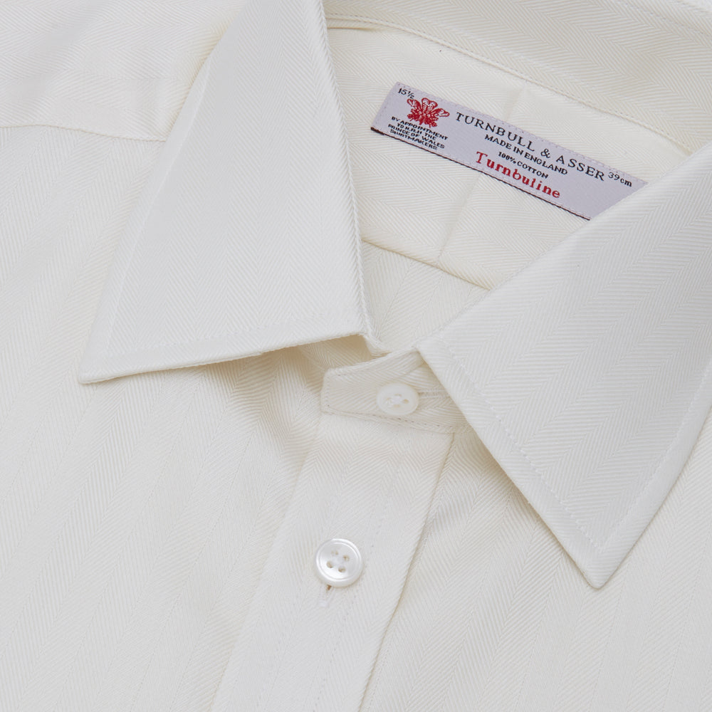 The Turnbull & Asser Cream Herringbone Superfine Cotton Shirt features a T&A collar and 3-button cuffs, ideal for minimalist style or bold ties, shown neatly folded against a plain white background.