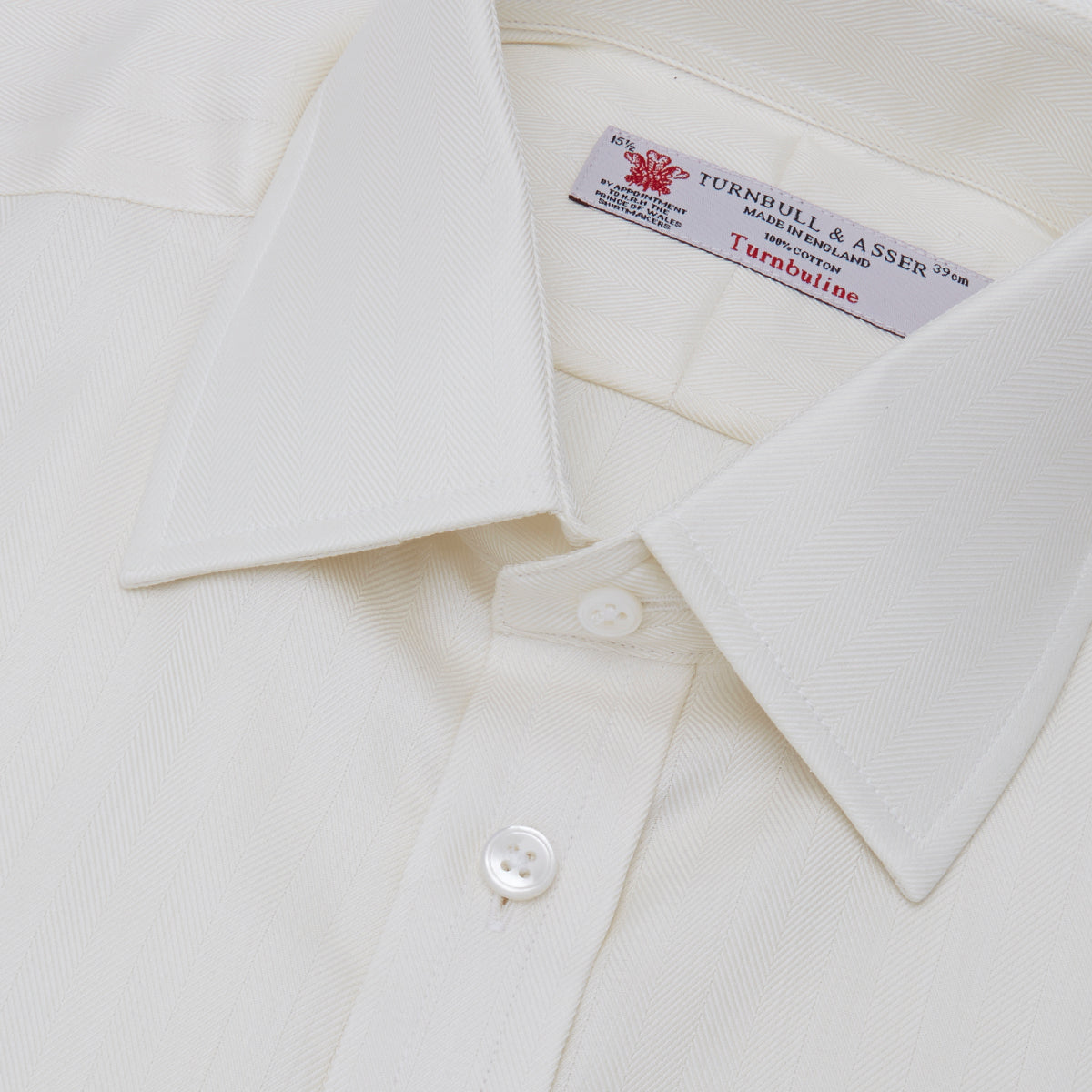 View 5 of product The Turnbull & Asser Cream Herringbone Superfine Cotton Shirt features a T&A collar and 3-button cuffs, ideal for minimalist style or bold ties, shown neatly folded against a plain white background.