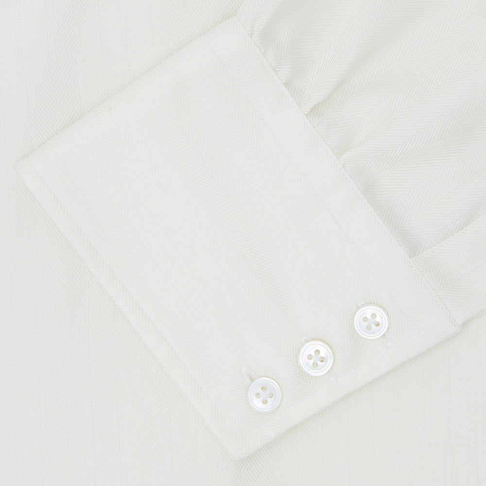 The Turnbull & Asser Cream Herringbone Superfine Cotton Shirt features a T&A collar and 3-button cuffs, ideal for minimalist style or bold ties, shown neatly folded against a plain white background.