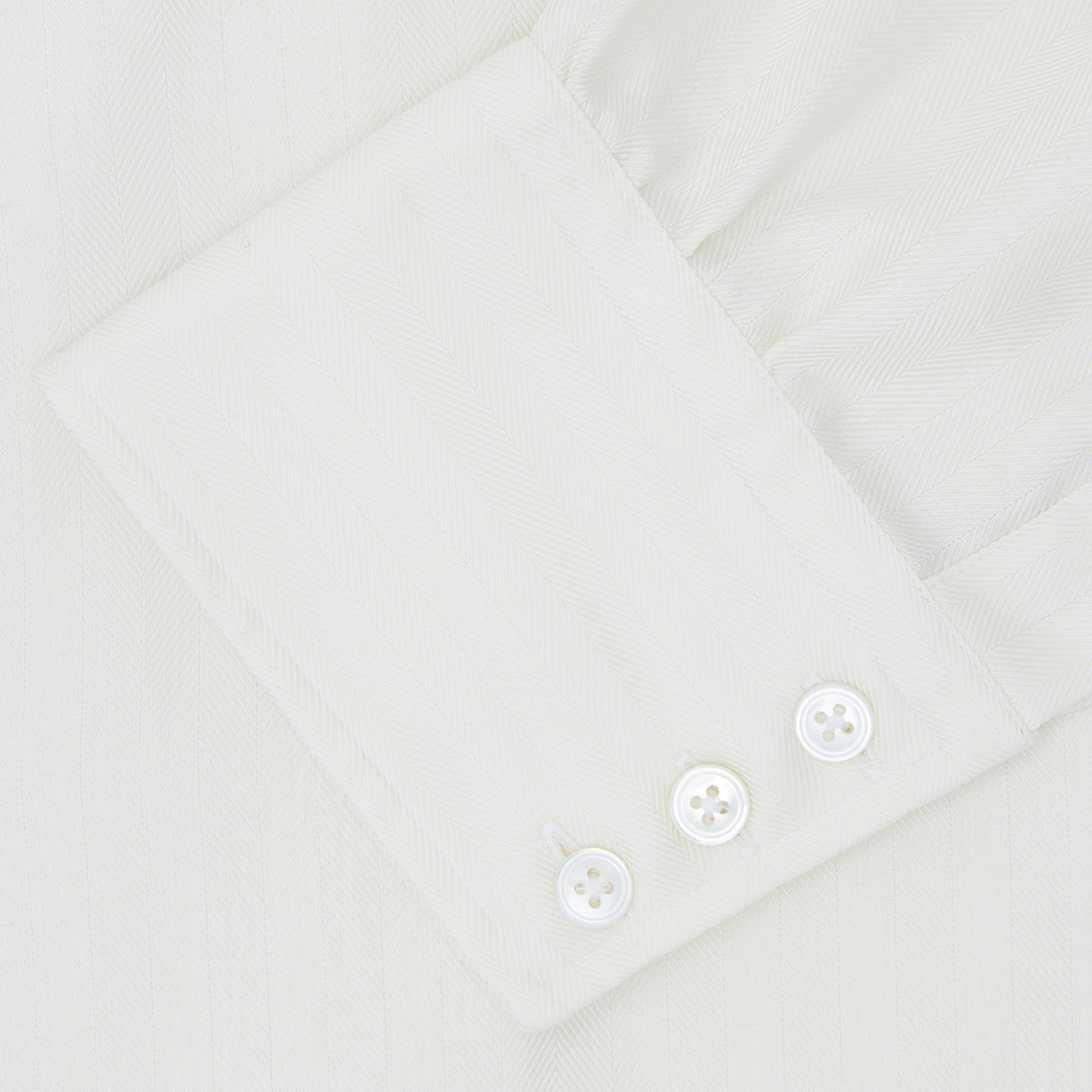 View 6 of product The Turnbull & Asser Cream Herringbone Superfine Cotton Shirt features a T&A collar and 3-button cuffs, ideal for minimalist style or bold ties, shown neatly folded against a plain white background.