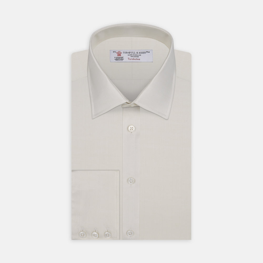 The Turnbull & Asser Cream Herringbone Superfine Cotton Shirt features a T&A collar and 3-button cuffs, ideal for minimalist style or bold ties, shown neatly folded against a plain white background.