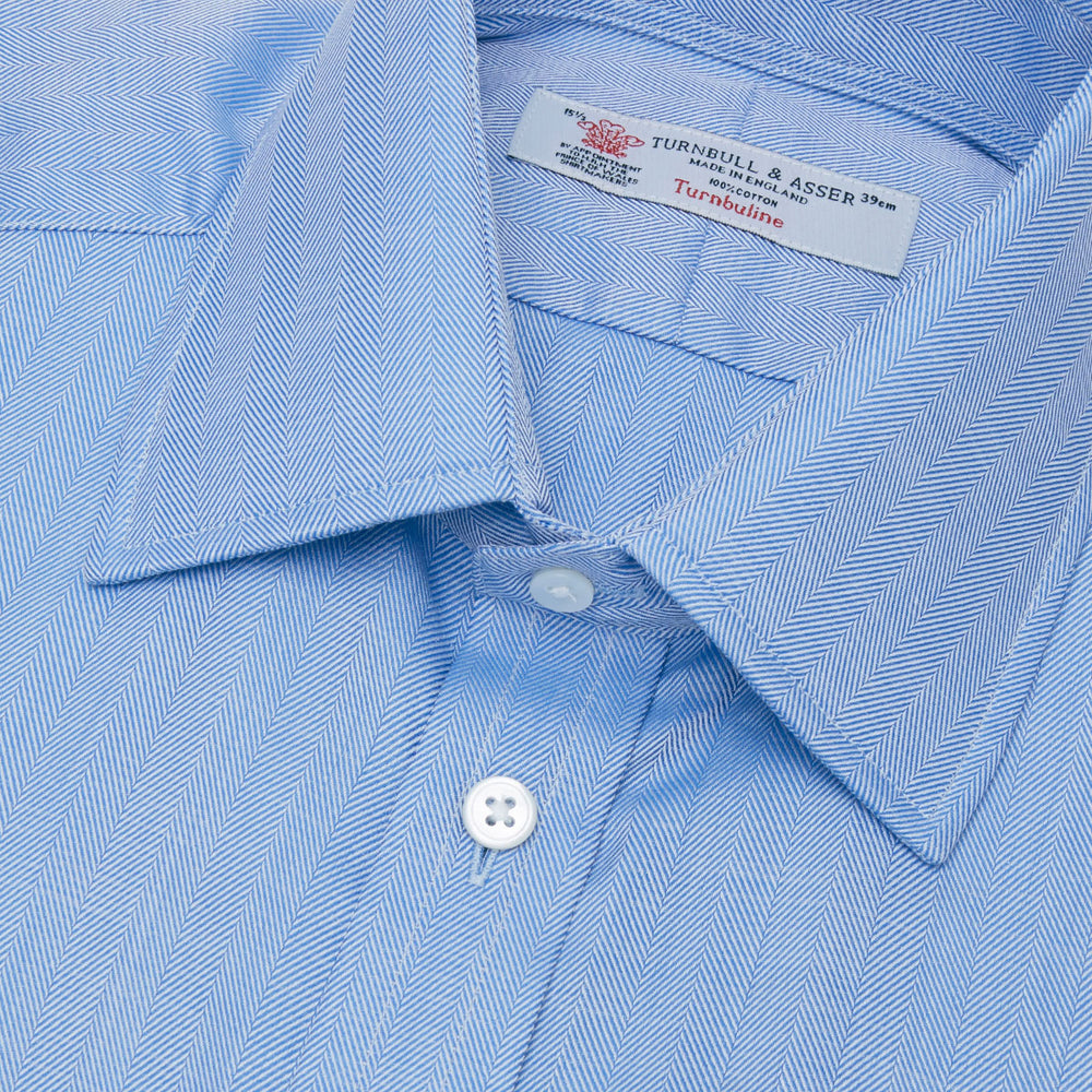 The Turnbull & Asser Blue Herringbone Superfine Cotton Shirt features a T&A collar and double cuffs—an essential for discerning gentlemen—shown folded on a plain white background.