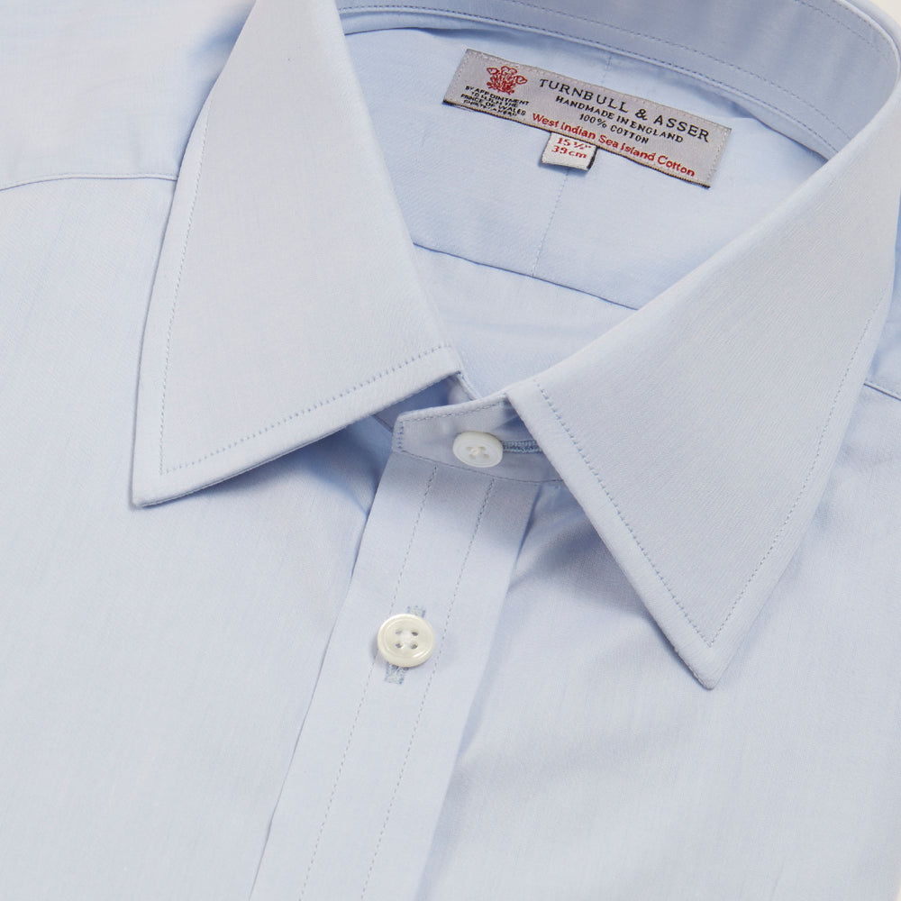 A neatly folded light blue long-sleeve dress shirt with a pointed collar and white buttons, styled with the Turnbull & Asser Monochrome Paisley Mill Silk Pocket Square (limited edition), displayed against a plain white background.