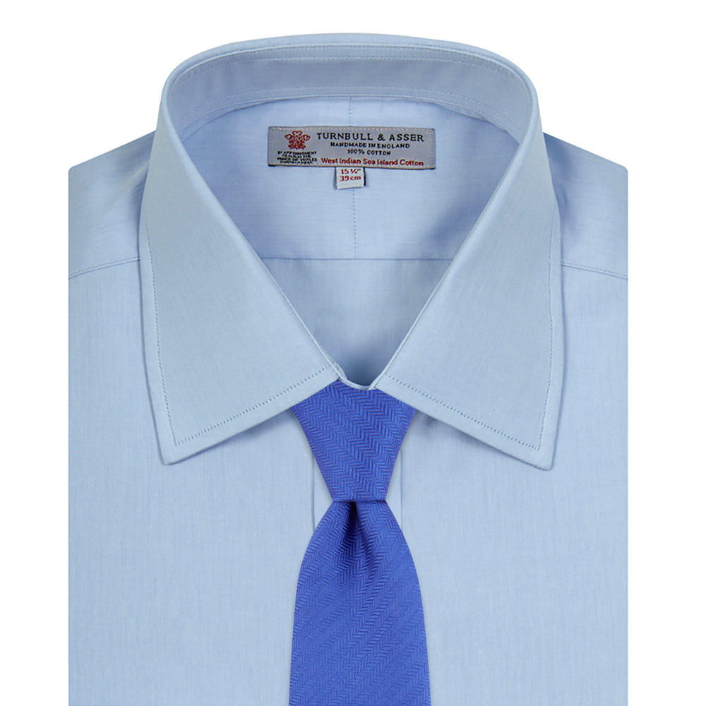 A neatly folded light blue long-sleeve dress shirt with a pointed collar and white buttons, styled with the Turnbull & Asser Monochrome Paisley Mill Silk Pocket Square (limited edition), displayed against a plain white background.