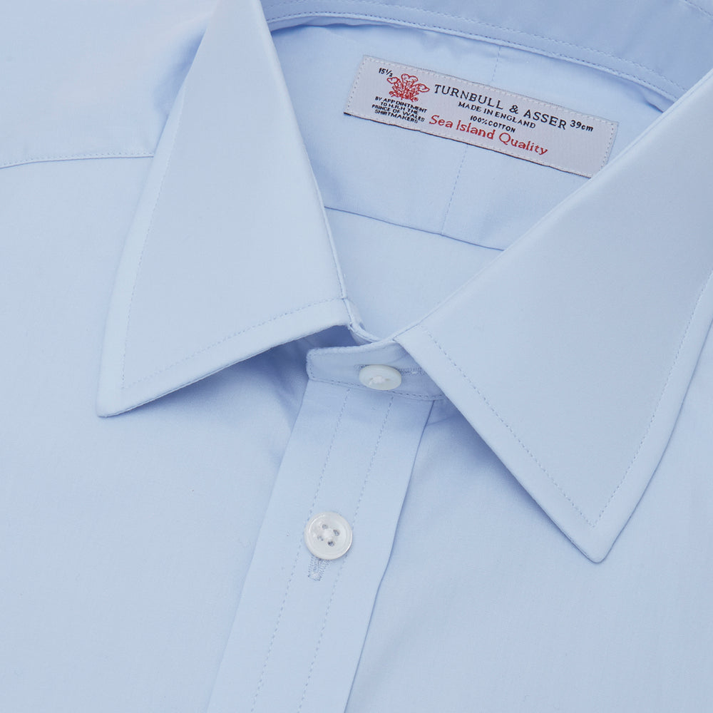 A neatly folded Light Blue Sea Island Quality Cotton Shirt by Turnbull & Asser, featuring a T&A collar and double cuffs, is displayed against a plain white background with the brand label visible inside the collar.