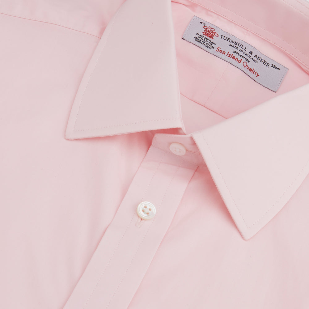 A slim black herringbone silk tie by Turnbull & Asser is paired with a neatly folded light pink long-sleeve dress shirt with a classic collar and white buttons, all displayed on a plain white background.