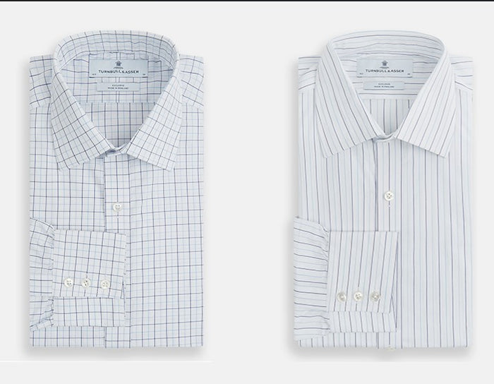 Two folded men’s dress shirts; the left shirt is white with a blue and red grid plaid pattern, and the right shirt is white with thin vertical blue stripes. Both have front pockets and buttoned cuffs.