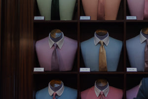 A display case showing mannequins dressed in pastel dress shirts and ties, each labeled with different collar styles, arranged neatly in individual cubbyholes.