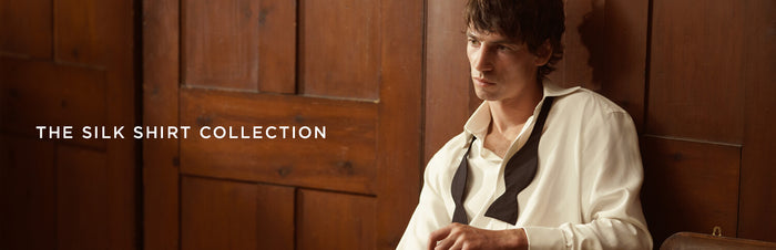 A man in a white silk shirt with a black necktie sits against a wooden paneled wall. Text on the image reads THE SILK SHIRT COLLECTION.