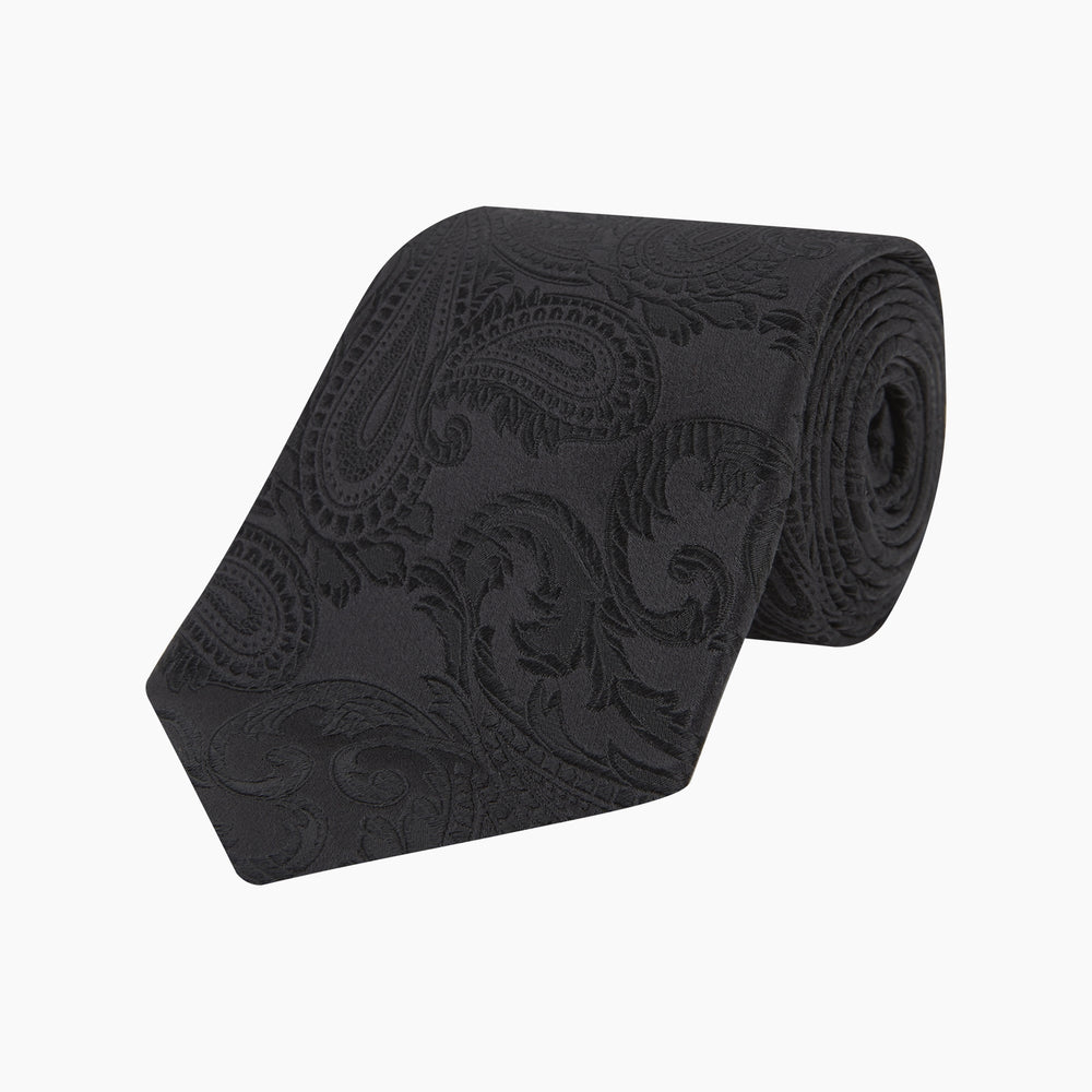 The Black Paisley Silk Tie by Turnbull & Asser features an elegant swirling paisley design with a subtle sheen—an all-black statement accessory photographed rolled up on a white background.