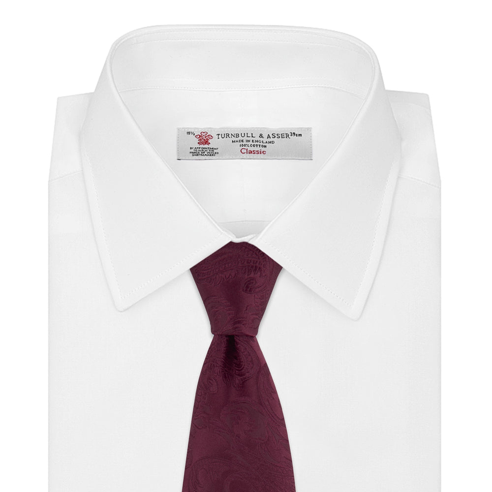 The Turnbull & Asser Burgundy Paisley Silk Tie, showcased rolled on a white background, is an elegant statement piece featuring a refined paisley design for any wardrobe.