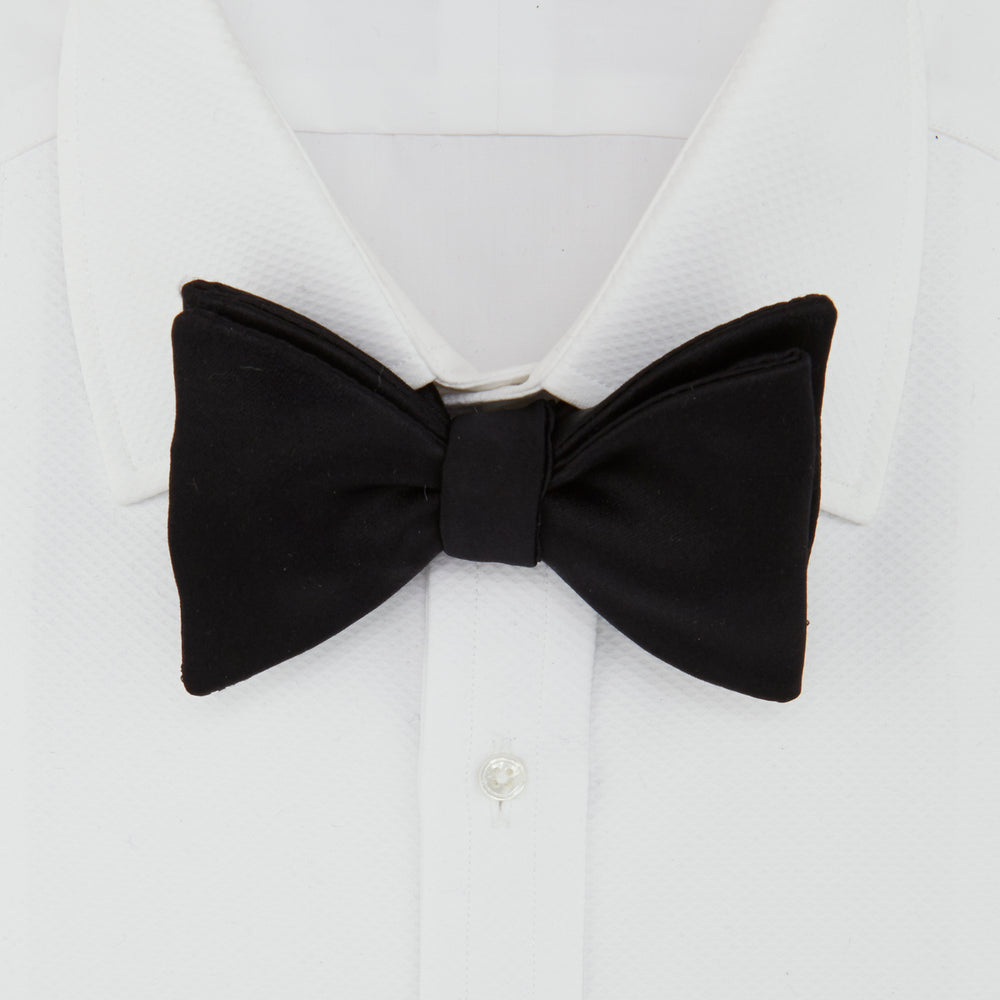 The Turnbull & Asser Black Satin Bow Tie features a classic, neatly tied shape, displayed on a white background—a sophisticated accessory for formal attire.