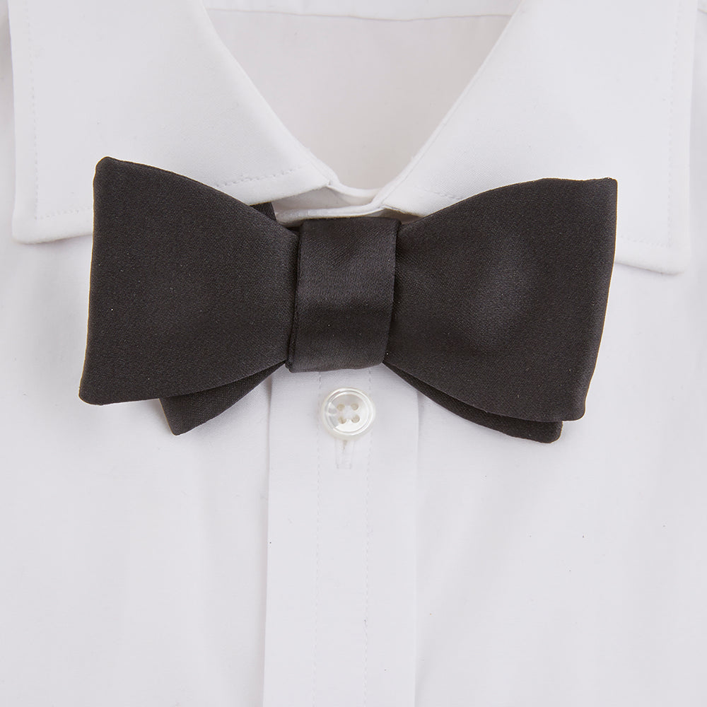 The Turnbull & Asser Black Silk Bow Tie features a matte finish and classic design, ideal for formal occasions. Shown pre-tied against a plain white background.