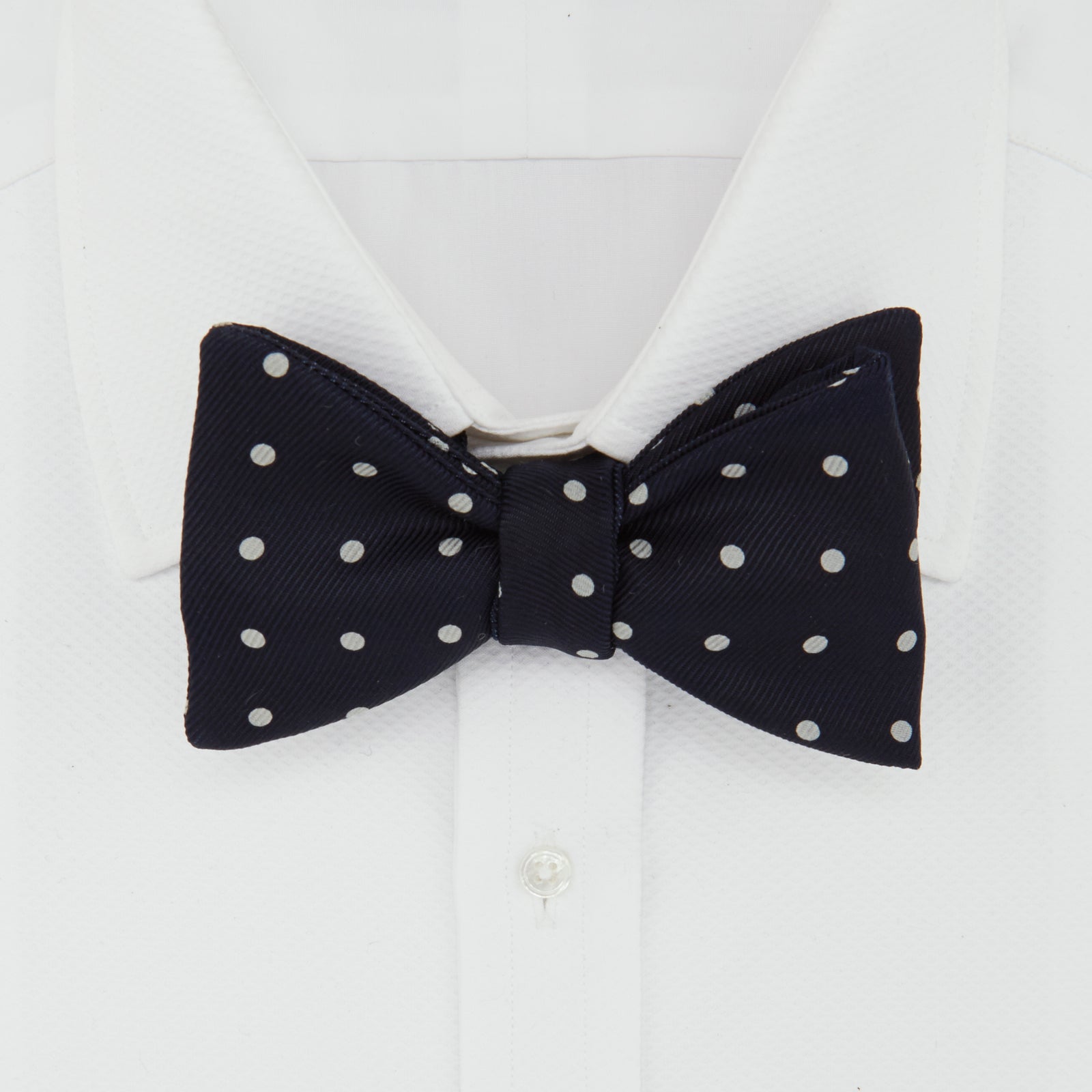 View 2 of product The Winston Navy and White Spot Silk Bow Tie by Turnbull & Asser features classic white polka dots on navy silk, reminiscent of Winston Churchill's style, and is shown against a plain white background.