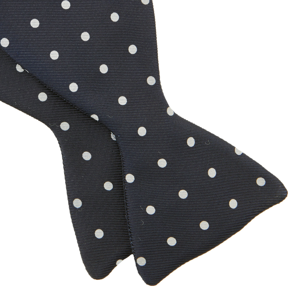 The Winston Navy and White Spot Silk Bow Tie by Turnbull & Asser features classic white polka dots on navy silk, reminiscent of Winston Churchill's style, and is shown against a plain white background.