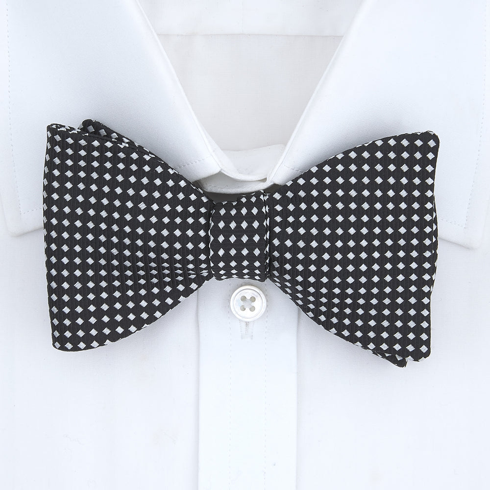 The Turnbull & Asser Diamond Black and White Silk Bow Tie features a black woven silk design with a tessellated diamond pattern of small white shapes, shown against a plain white background.