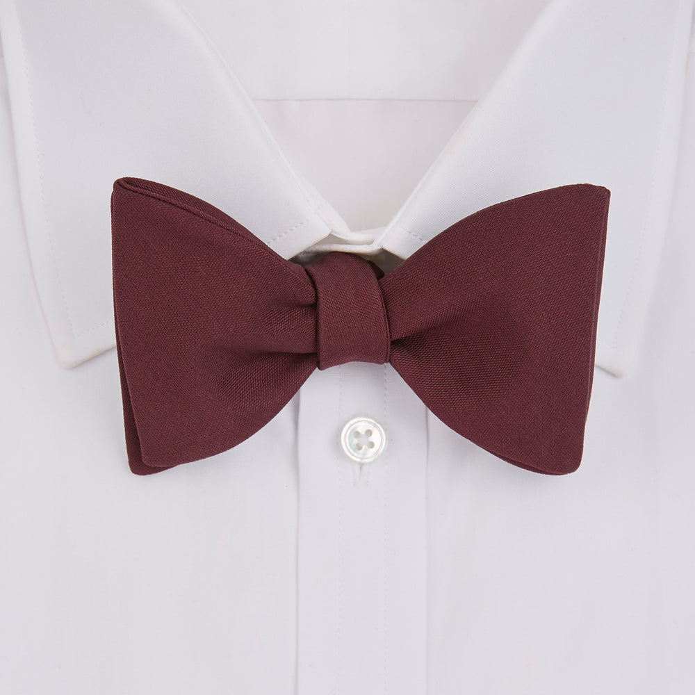 The Turnbull & Asser Burgundy Barathea Bow Tie, shown neatly tied with pointed ends on a white background, features smooth matte fabric for a refined formal look.