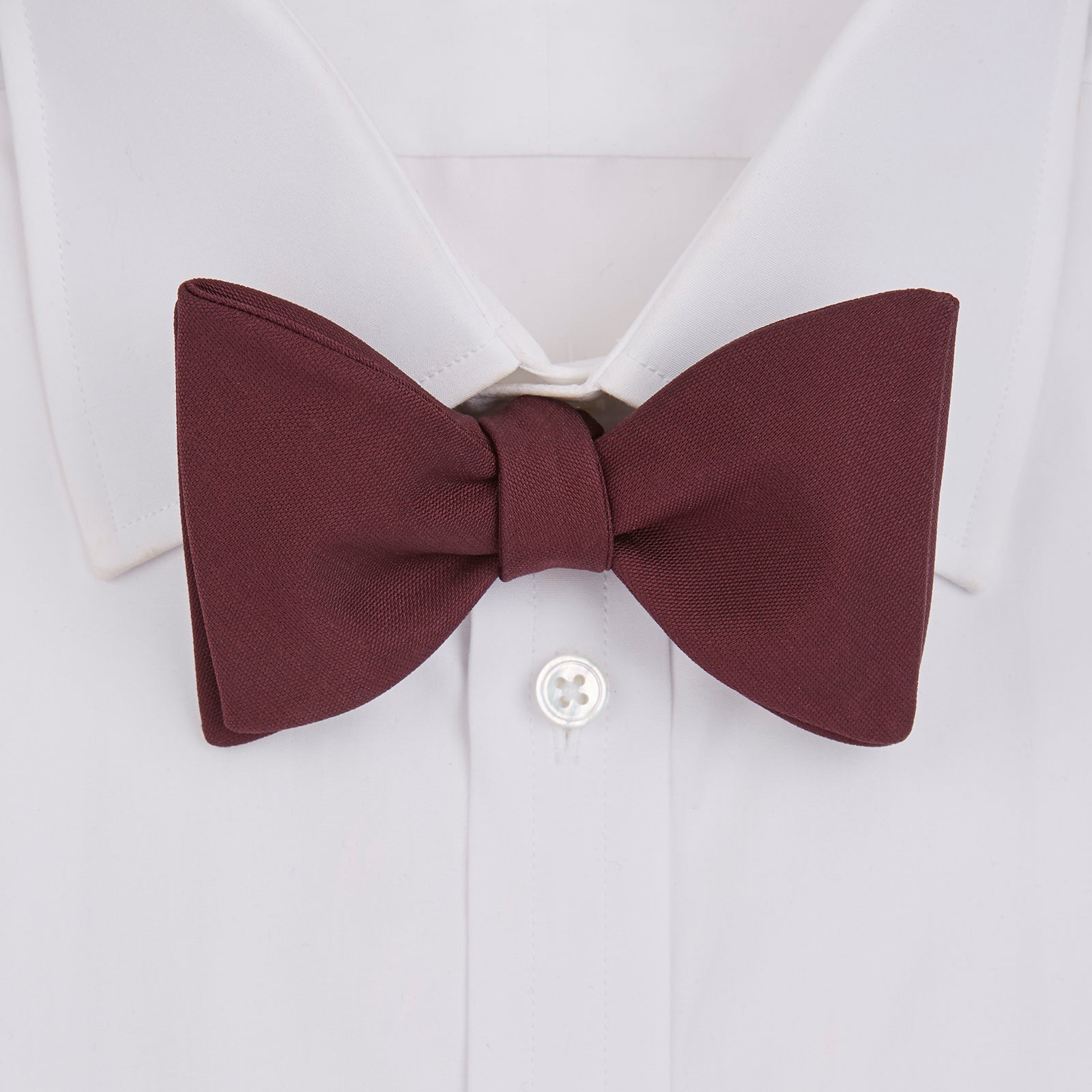 View 2 of product The Turnbull & Asser Burgundy Barathea Bow Tie, shown neatly tied with pointed ends on a white background, features smooth matte fabric for a refined formal look.