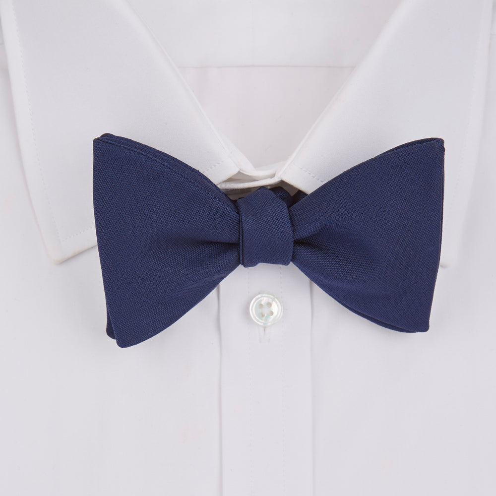 The Turnbull & Asser Navy Barathea Bow Tie features a classic butterfly shape in deep blue silk, ideal for formal occasions, shown against a white background.