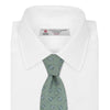 View 2 of product The Turnbull & Asser Green Star Flowers Silk Tie features a light green jacquard with a subtle checkered pattern and small blue star flower motifs, shown rolled up on a white background.
