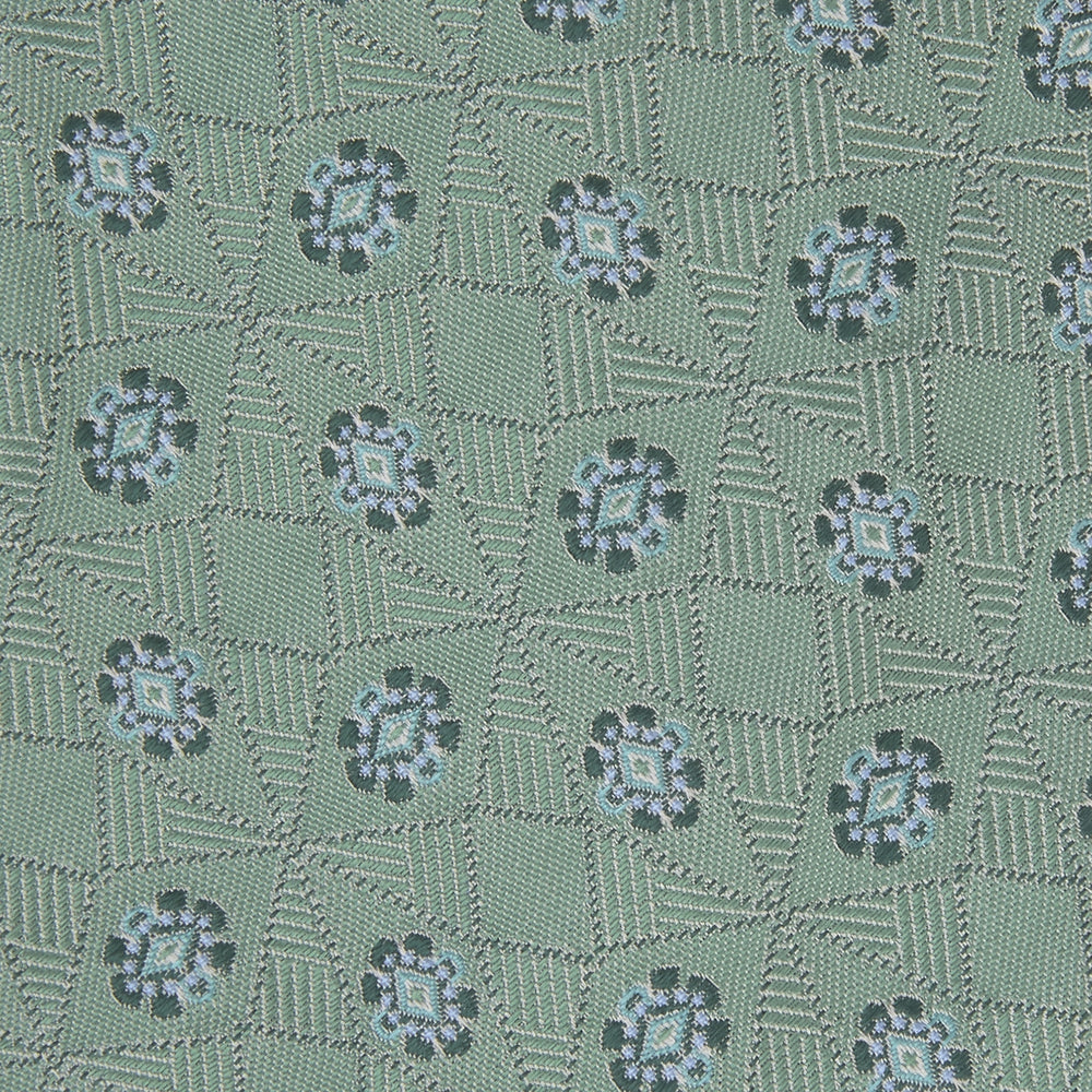 The Turnbull & Asser Green Star Flowers Silk Tie features a light green jacquard with a subtle checkered pattern and small blue star flower motifs, shown rolled up on a white background.