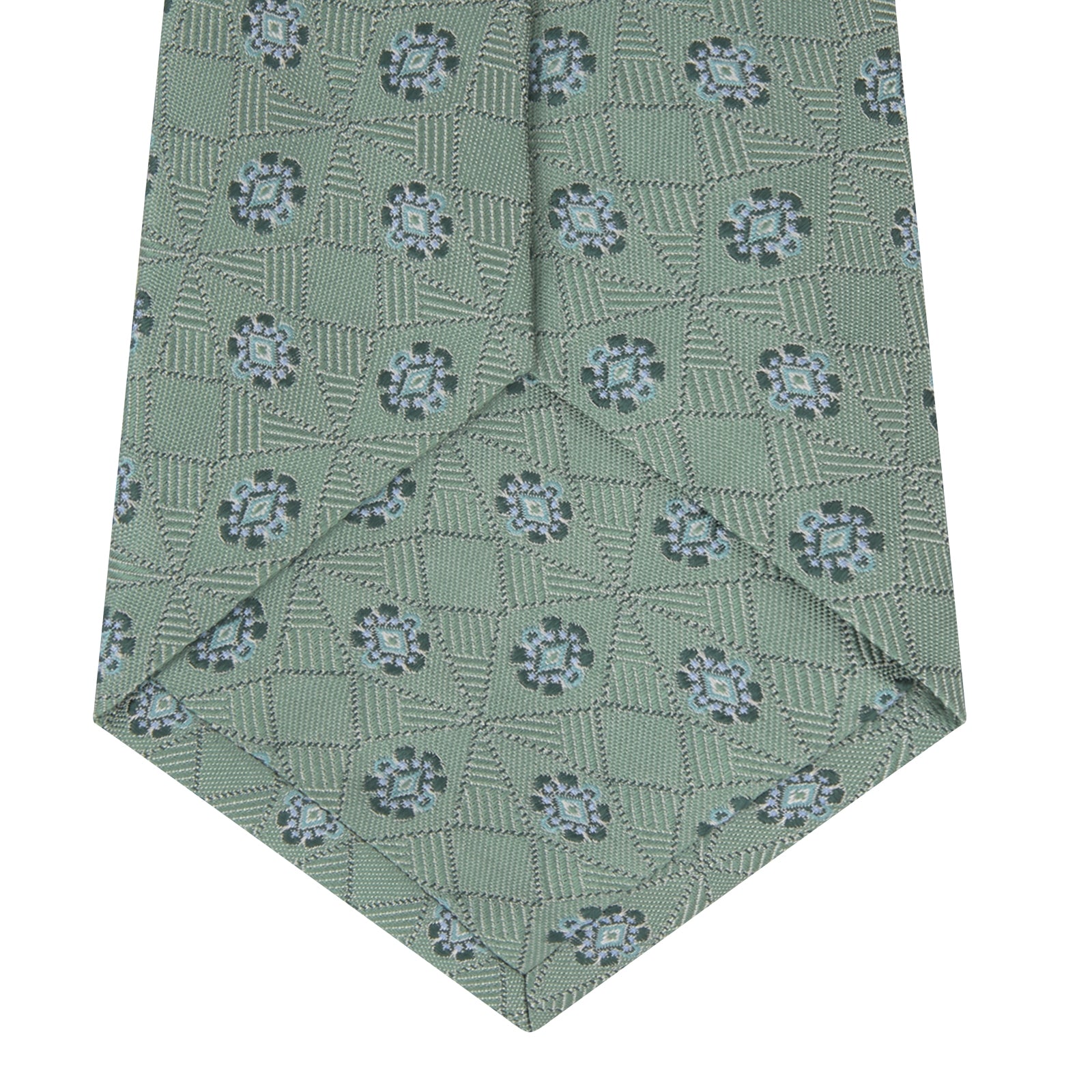 View 4 of product The Turnbull & Asser Green Star Flowers Silk Tie features a light green jacquard with a subtle checkered pattern and small blue star flower motifs, shown rolled up on a white background.