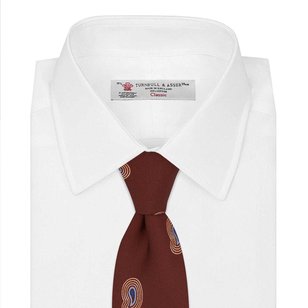 The Turnbull & Asser Red Pulse Paisley Silk Tie features a rolled red silk design with a repeating pattern of tan, blue, and white abstract pulse motifs.