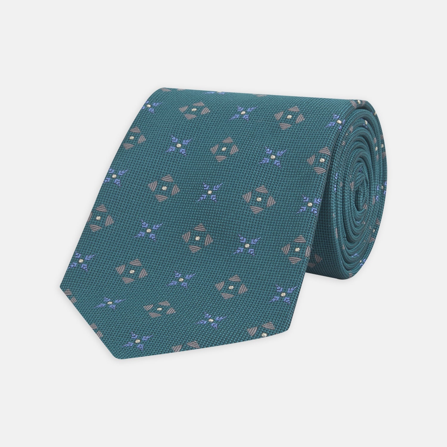 View 1 of product The Turquoise Crosses Silk Tie by Turnbull & Asser features a subtle geometric motif in tan and blue, displayed rolled on a white background—ideal for the modern office.