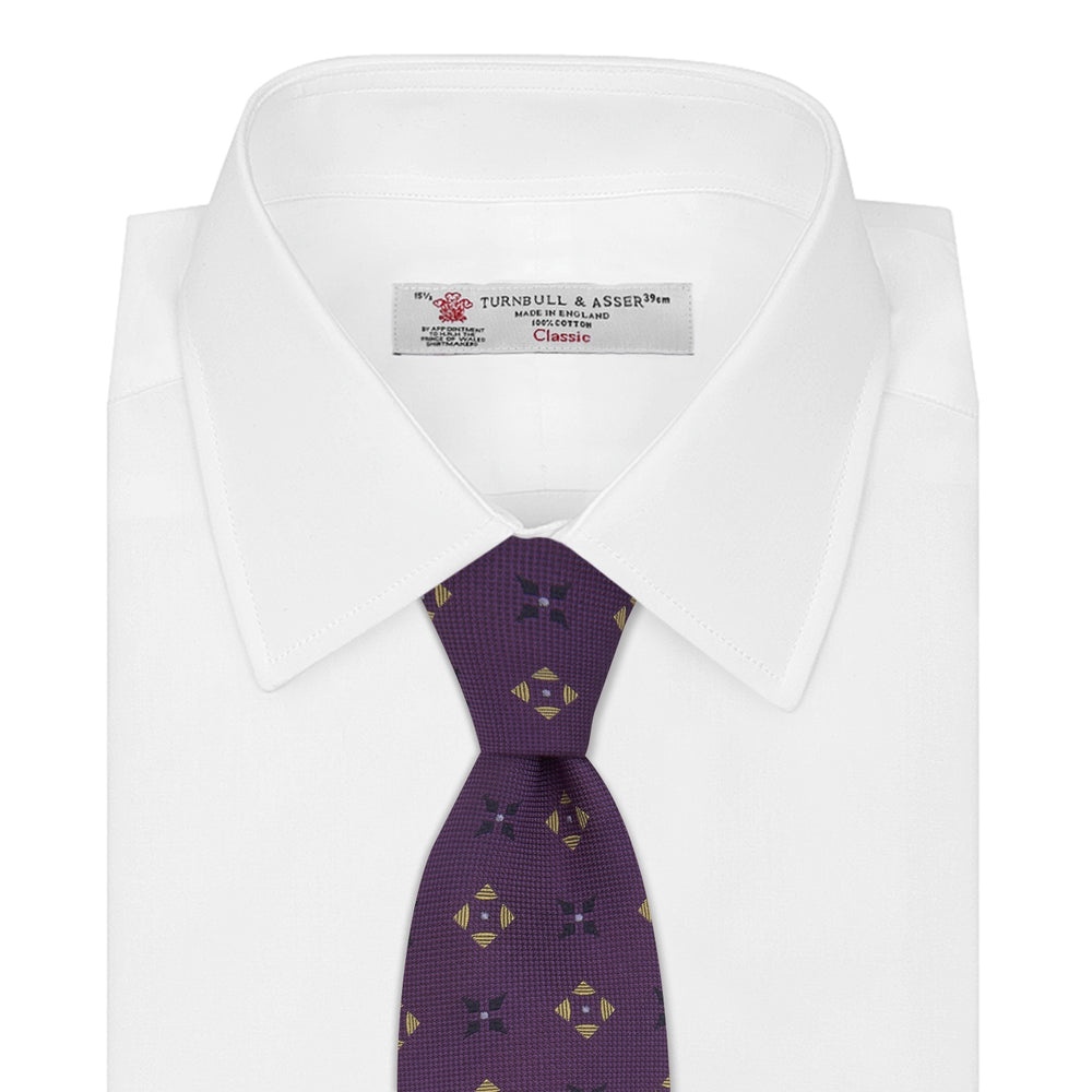 The Turnbull & Asser Purple Crosses Silk Tie features a rolled-up purple design with small yellow and black cross motifs on silk.