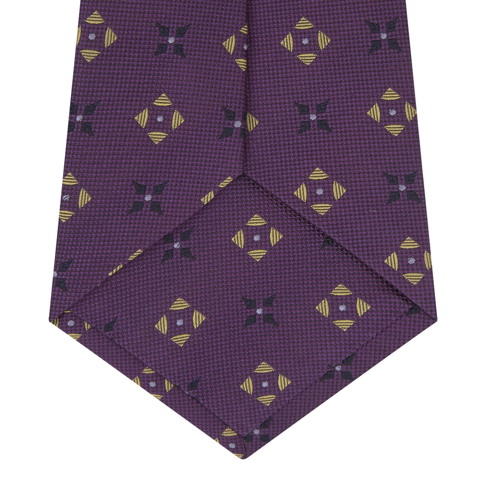 The Turnbull & Asser Purple Crosses Silk Tie features a rolled-up purple design with small yellow and black cross motifs on silk.