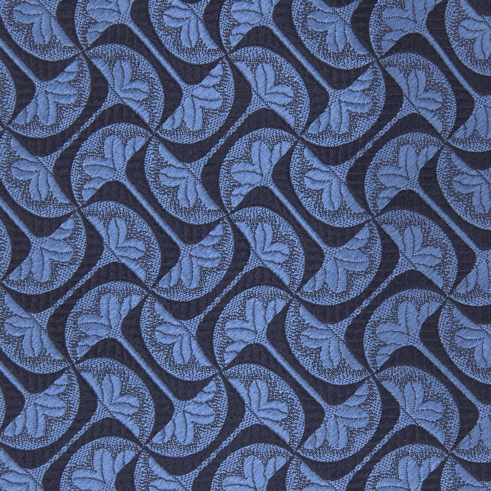 The Turnbull & Asser Blue Geo Silk Tie features a refined blue silk with a light blue abstract leaf pattern in a geometric design, rolled at one end and shown on a plain white background.