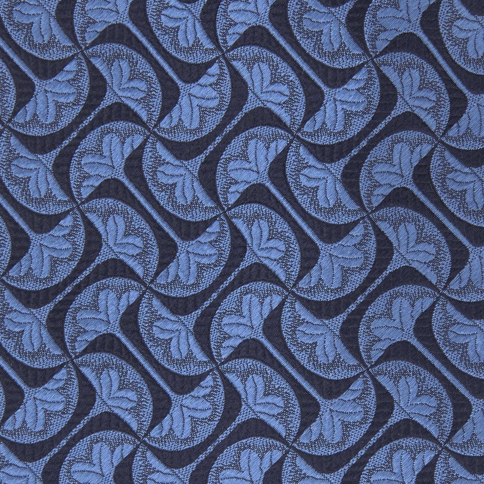 View 3 of product The Turnbull & Asser Blue Geo Silk Tie features a refined blue silk with a light blue abstract leaf pattern in a geometric design, rolled at one end and shown on a plain white background.