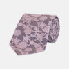View 1 of product The Turnbull & Asser Pink Floral Occasion Silk Tie features a rolled-up purple jacquard design with a light pink floral pattern, perfect for weddings or floral events, shown on a plain white background.