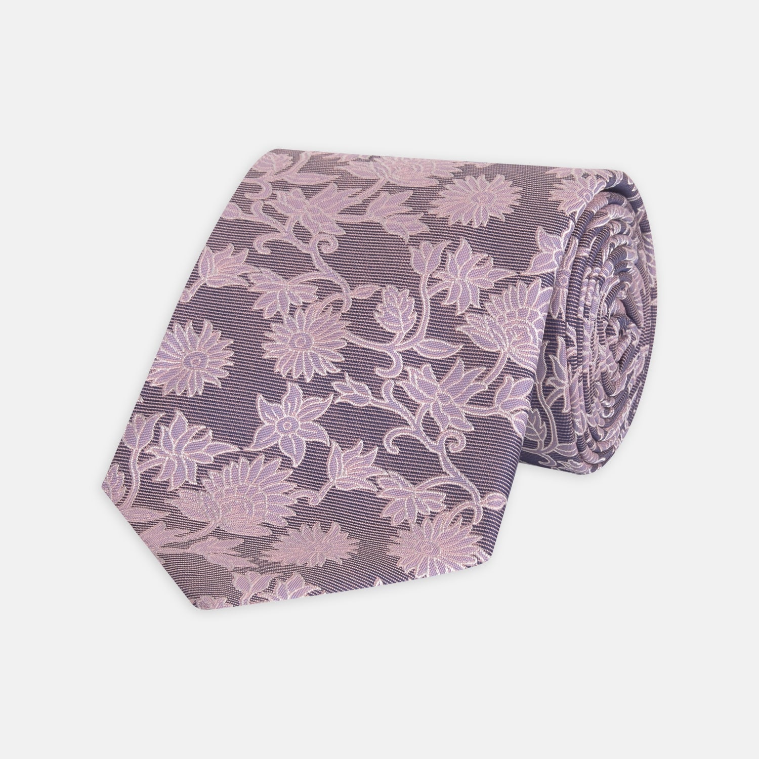 View 1 of product The Turnbull & Asser Pink Floral Occasion Silk Tie features a rolled-up purple jacquard design with a light pink floral pattern, perfect for weddings or floral events, shown on a plain white background.