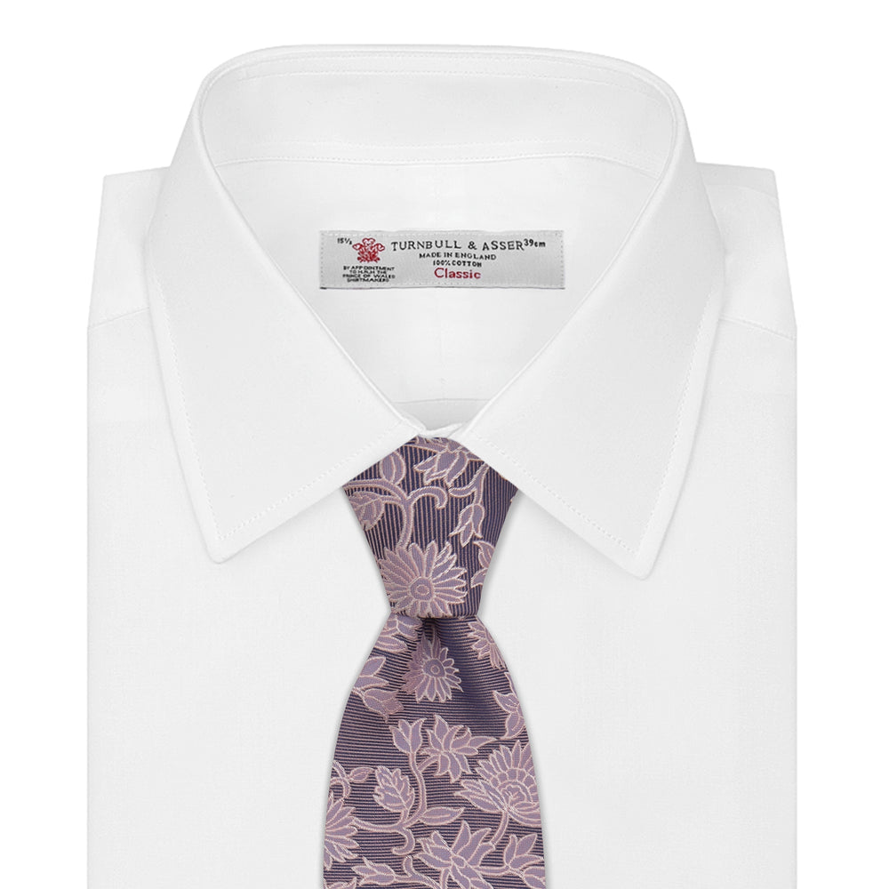 The Turnbull & Asser Pink Floral Occasion Silk Tie features a rolled-up purple jacquard design with a light pink floral pattern, perfect for weddings or floral events, shown on a plain white background.