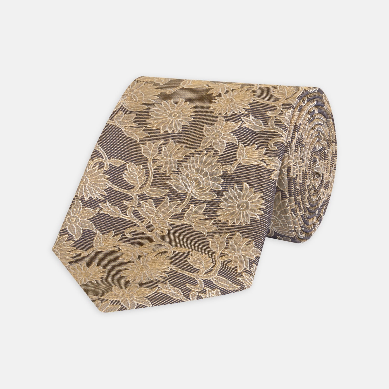 View 1 of product The Copper Floral Occasion Silk Tie by Turnbull & Asser features a gold floral jacquard pattern on brown silk, elegantly rolled on a white surface—an ideal choice for weddings.
